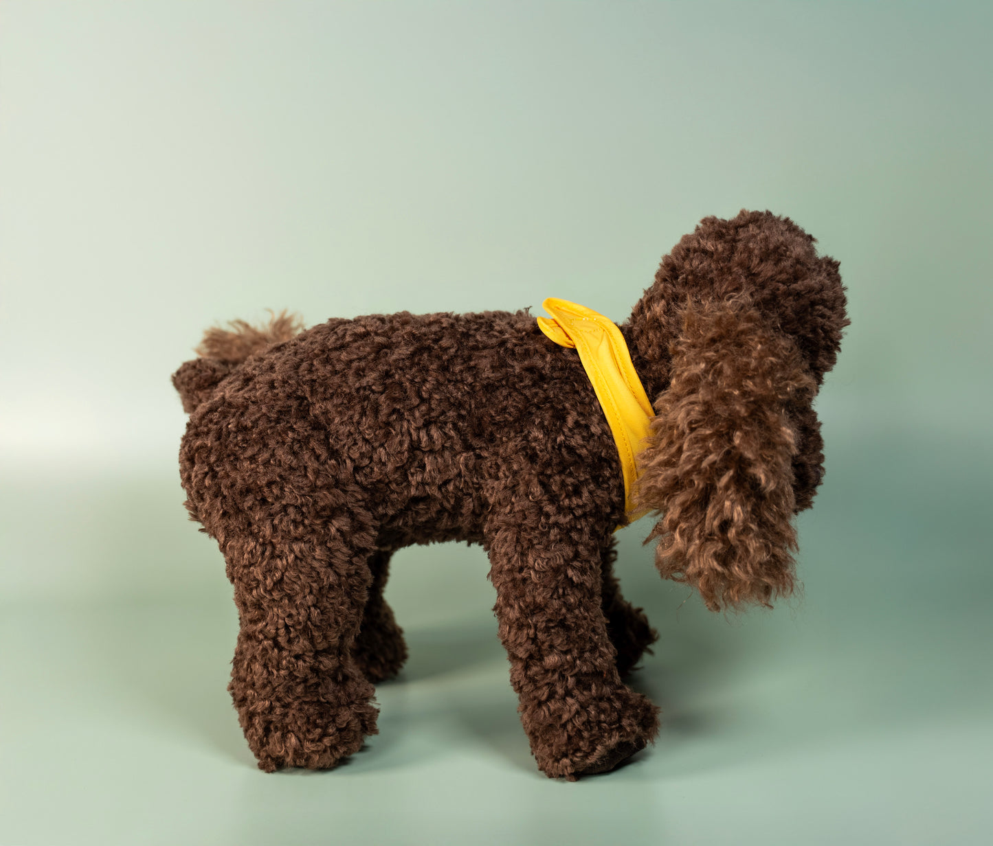 Brown dog plush toy with a yellow bandana on a light grey background