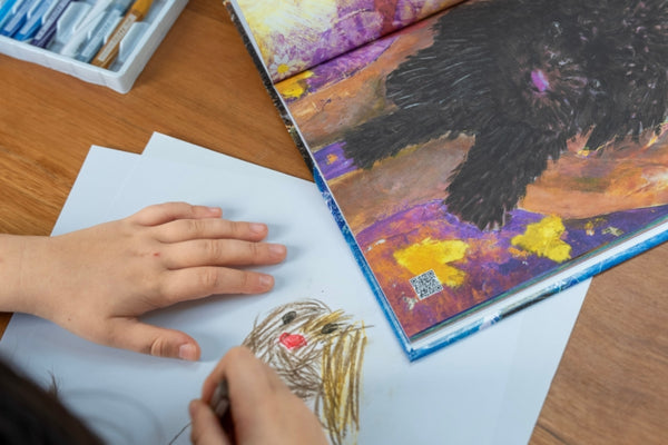 A child drawing beside an illustrated Kitty and Raffy storybook