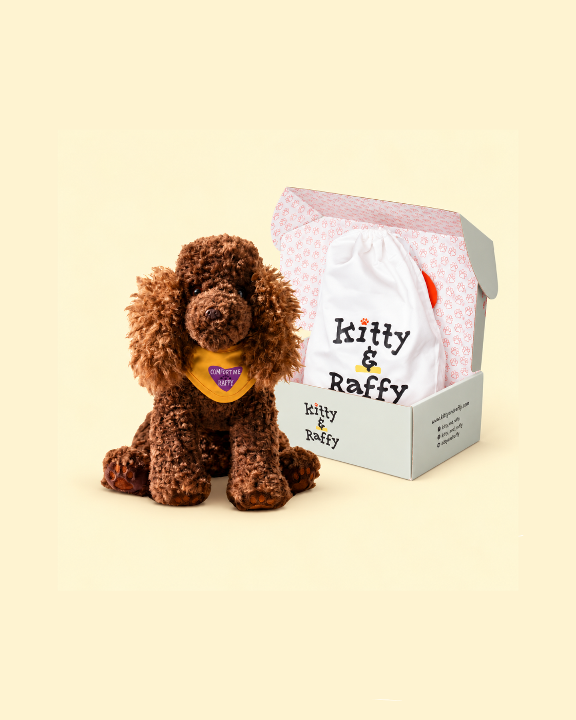 A brown curly-haired plush dog toy sits beside an open branded gift box containing a white drawstring bag printed with 'Kitty & Raffy' on a warm cream background.
