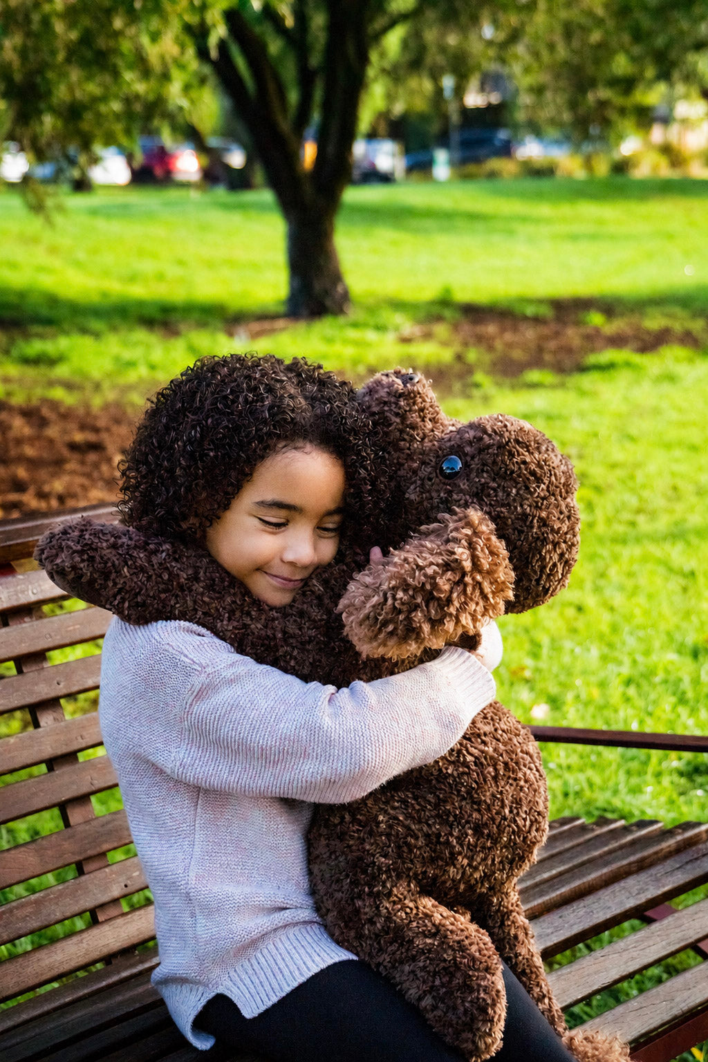 A child cuddling Hug Me Raffy on a park bench
