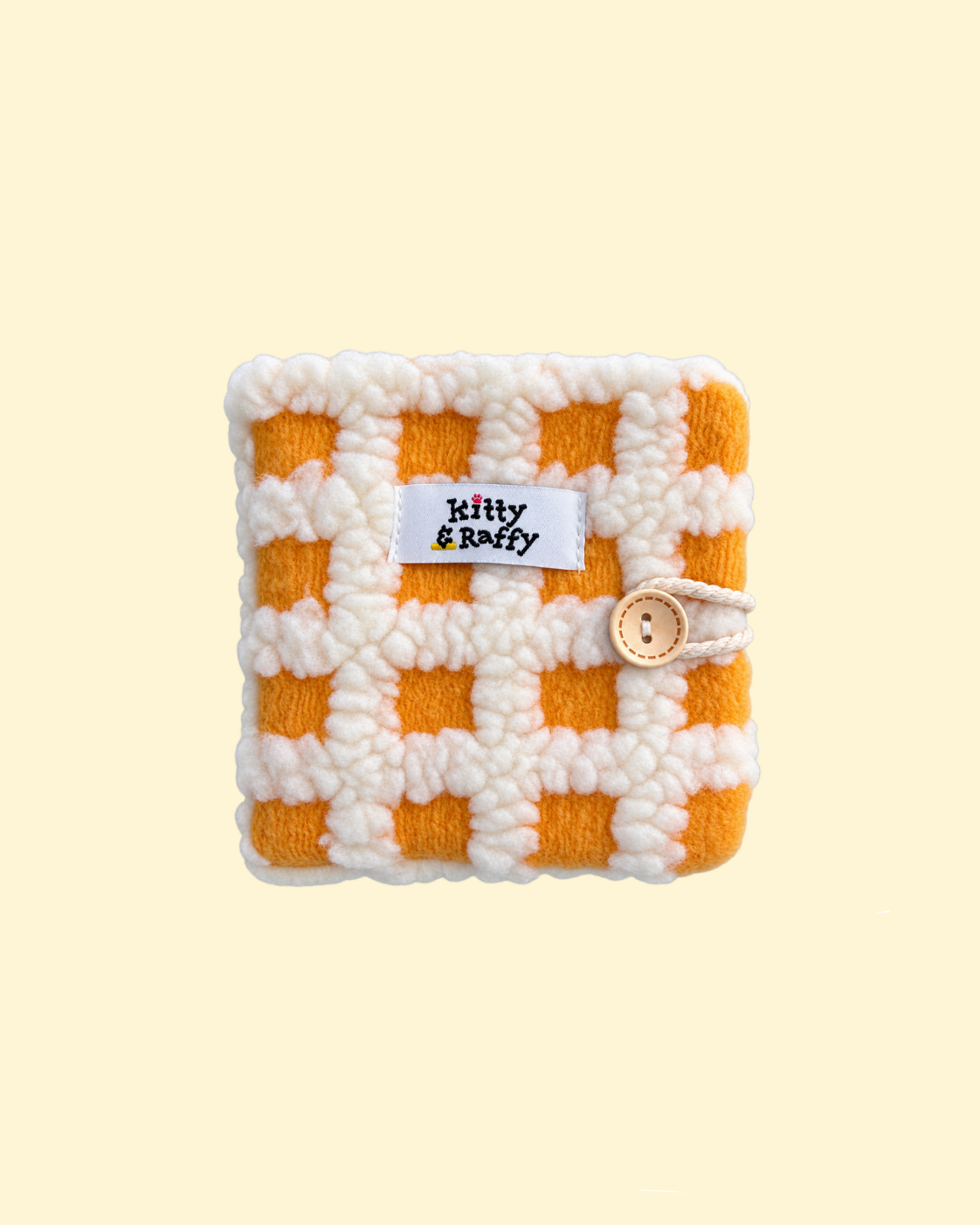 A small yellow photo album with a white and orange checkered pattern, featuring a white fabric label that reads 'Kitty & Raffy' and a small wooden button closure. Store precious memories here!